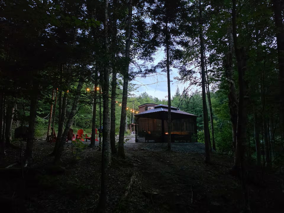 Tiny house and gazebo lit up at dusk from the forest